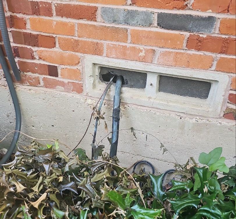 Refrigerant line entering near ground level on an East Dallas pier-and-beam home, showing it was routed beneath the house rather than beneath the roof deck.