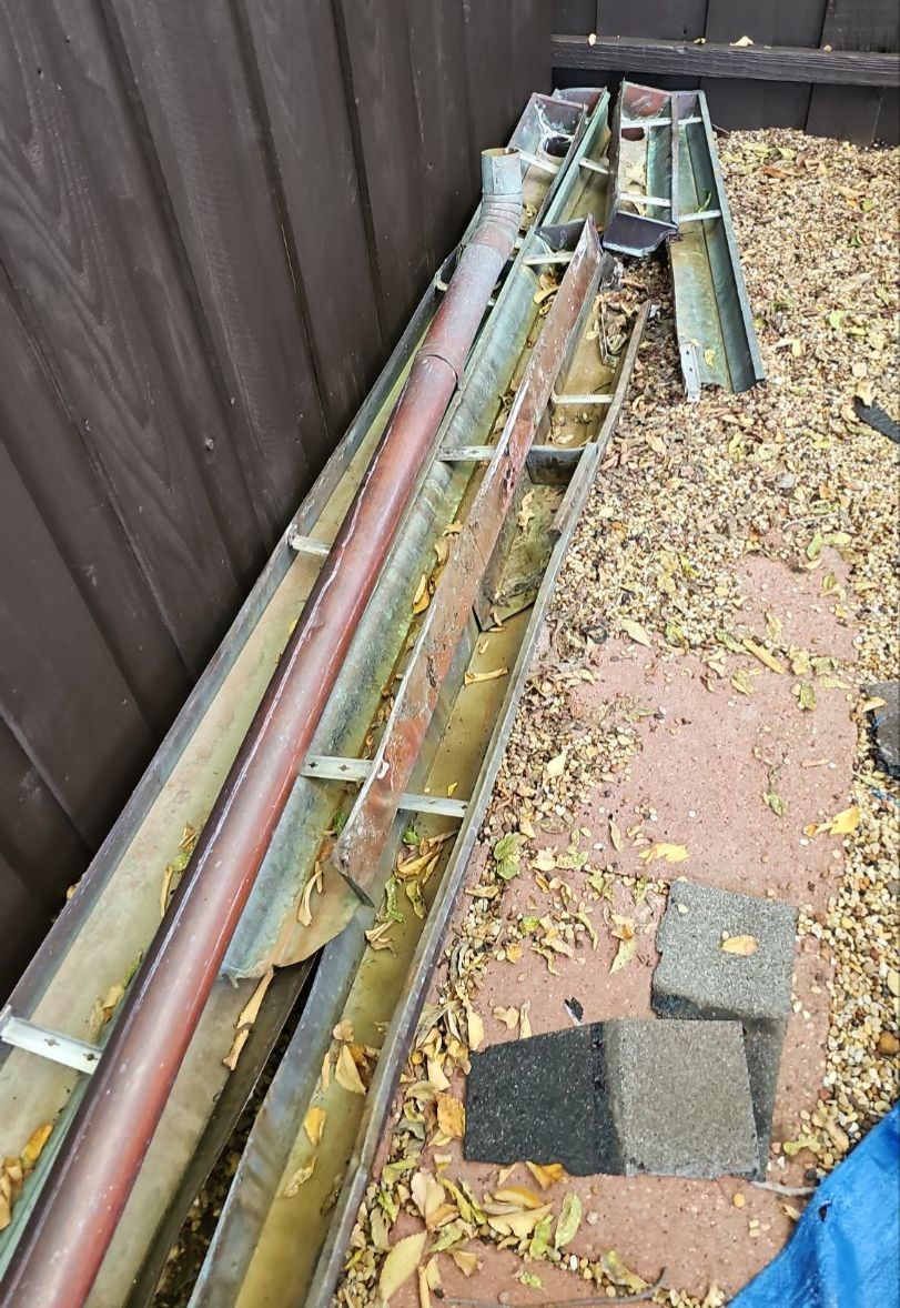 Sections of original copper gutters temporarily removed and stored beside a fence during a roof replacement in Preston Hollow, Dallas.