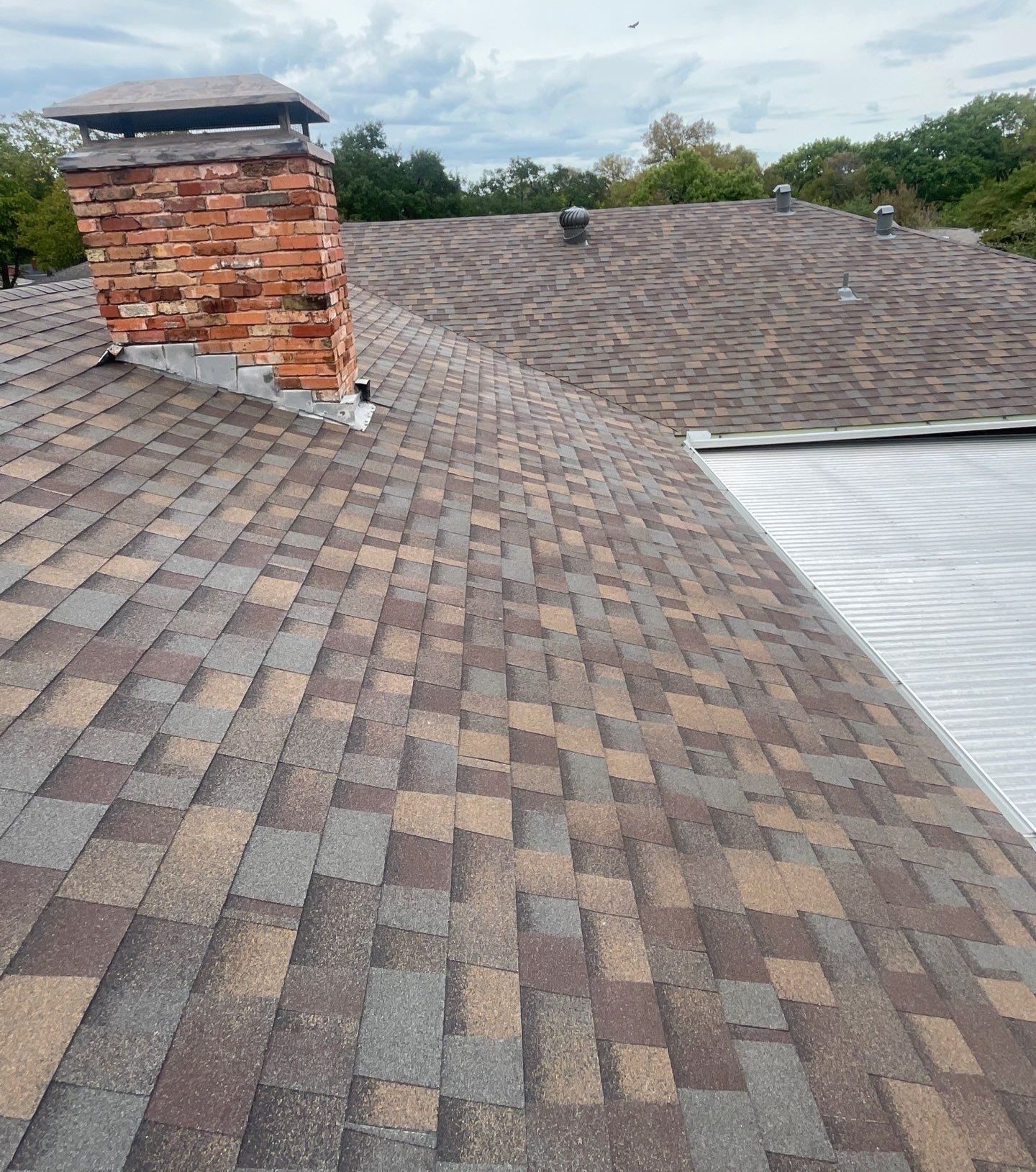Newly installed Owens Corning Duration Teak shingles on an East Dallas roof, showing the brown color variation and brick chimney.